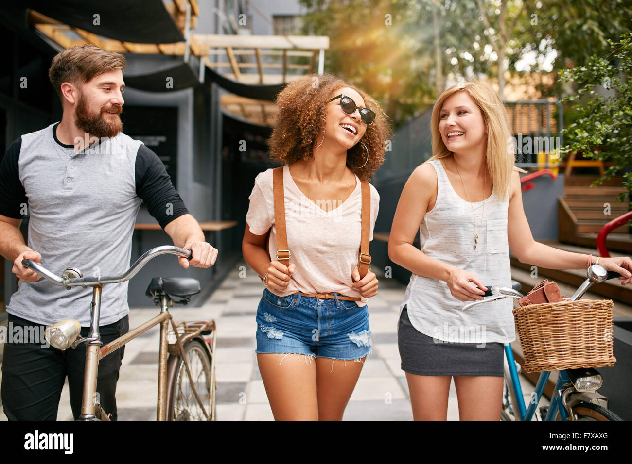 Glückliche junge Leute hinunter die Stadtstraße mit ihren Fahrrädern und lächelnd. Junge Menschen und Frauen mit ihren Fahrrädern unterwegs. Stockfoto