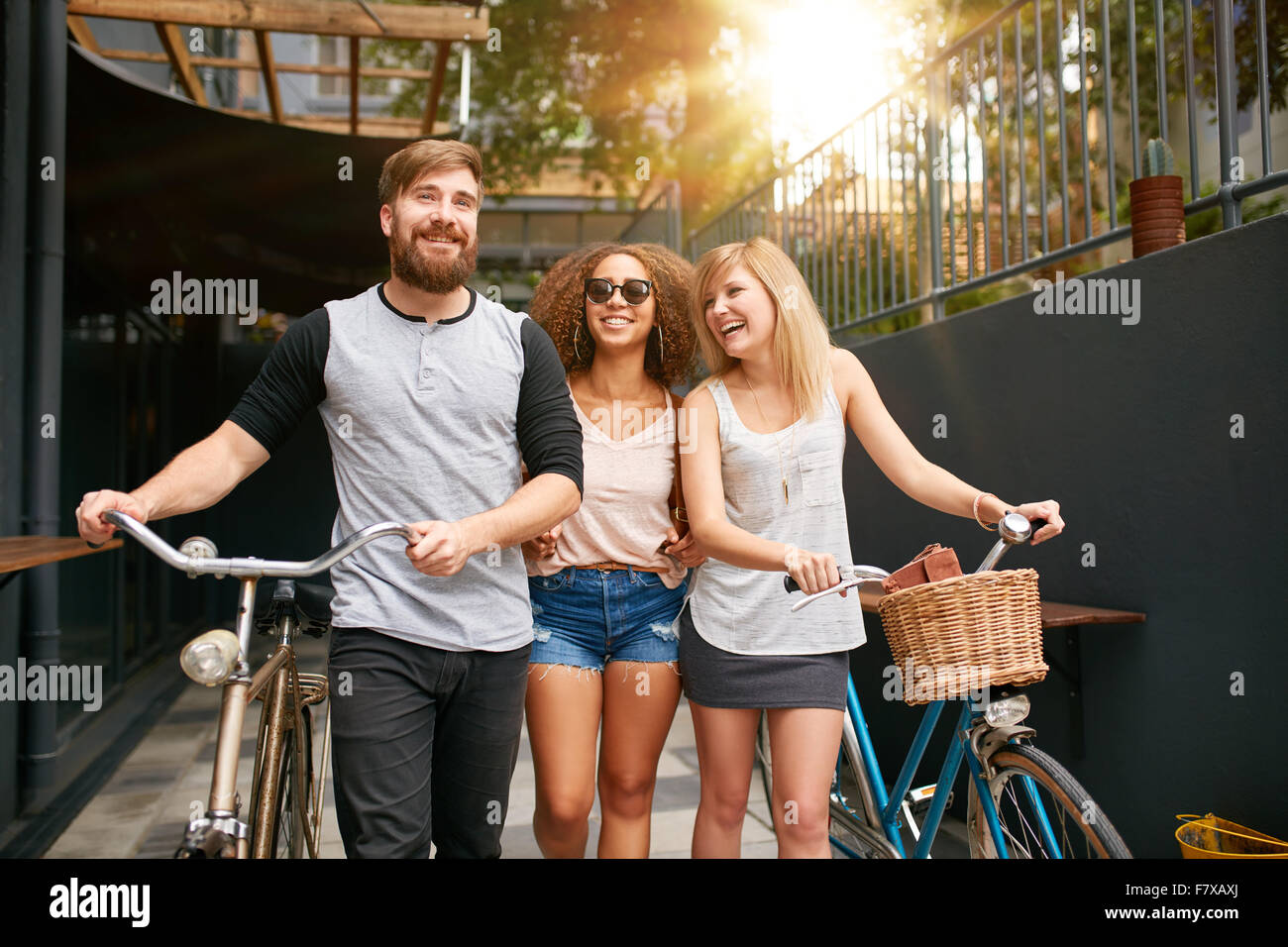 Drei junge Menschen zu Fuß auf der Straße mit ihren Fahrrädern und Spaß haben. Männliche und weibliche Freunde mit ihrem Fahrrad auf Stadt-s Stockfoto
