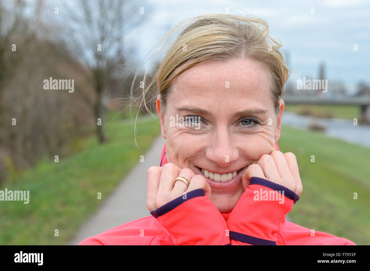 Sportlich im mittleren Alter blonde Frau auf dem Deich und Lächeln verschmitzt in die Kamera. Stockfoto