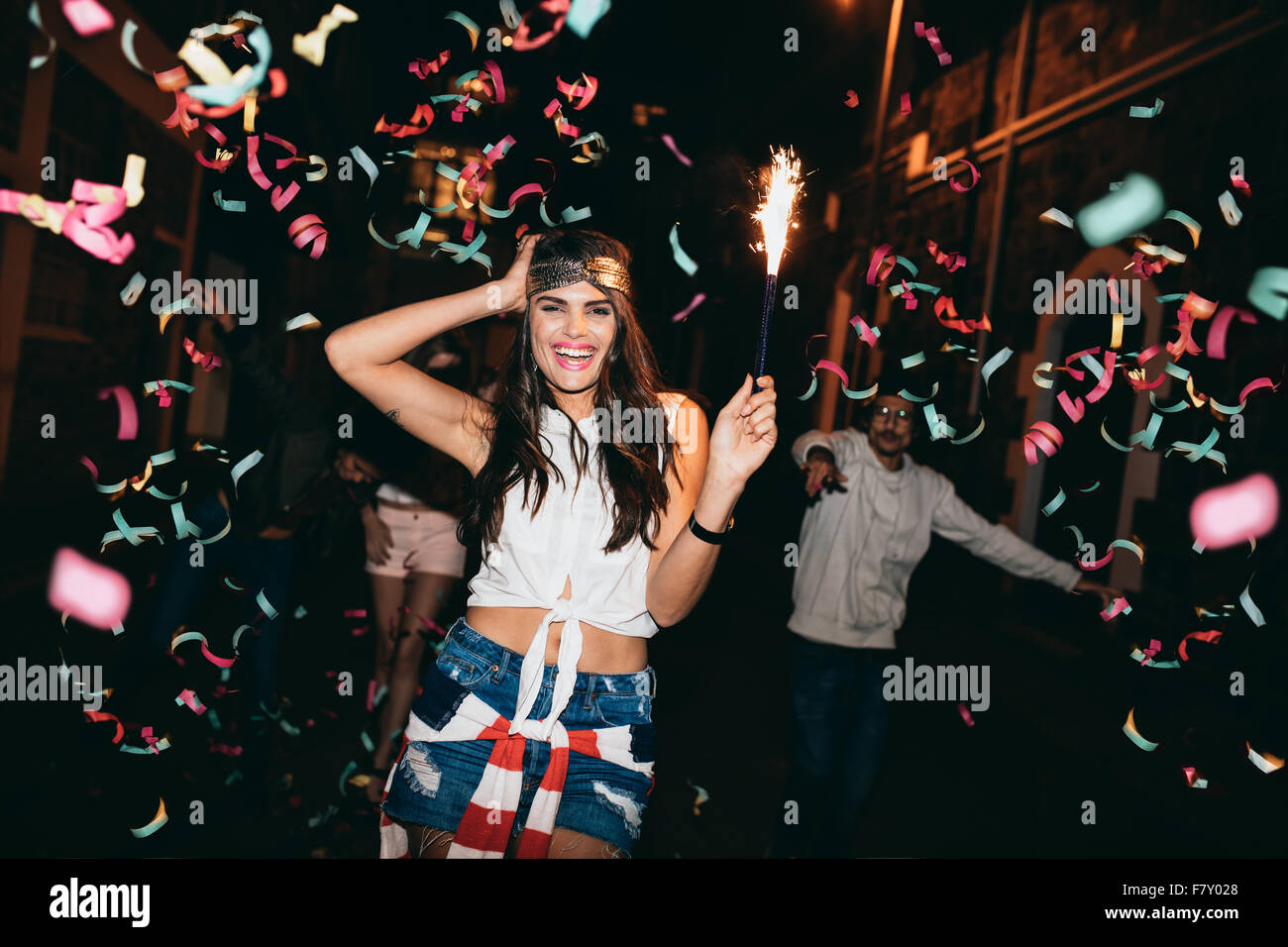 Glückliche junge Frau feiern mit ihren Freunden im Freien in der Nacht. Freunde, Partys im Freien mit Konfetti und Wunderkerzen. Stockfoto