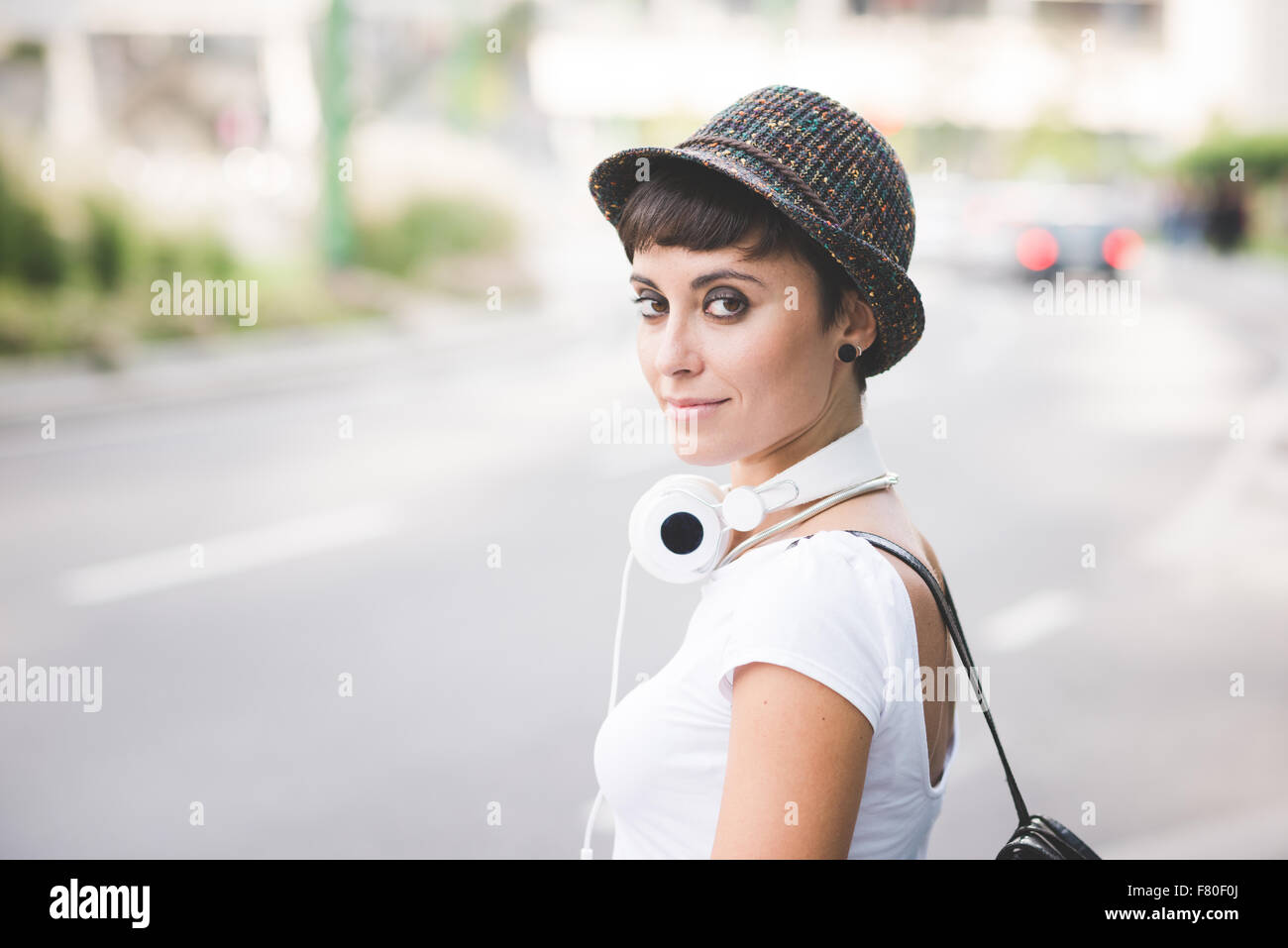 Halbe Länge des jungen schönen kaukasischen braun glattes Haar Frau mit Kopfhörer um den Hals, auf der Suche in der Kamera - heiter - unbeschwerte, Musikkonzept Stockfoto