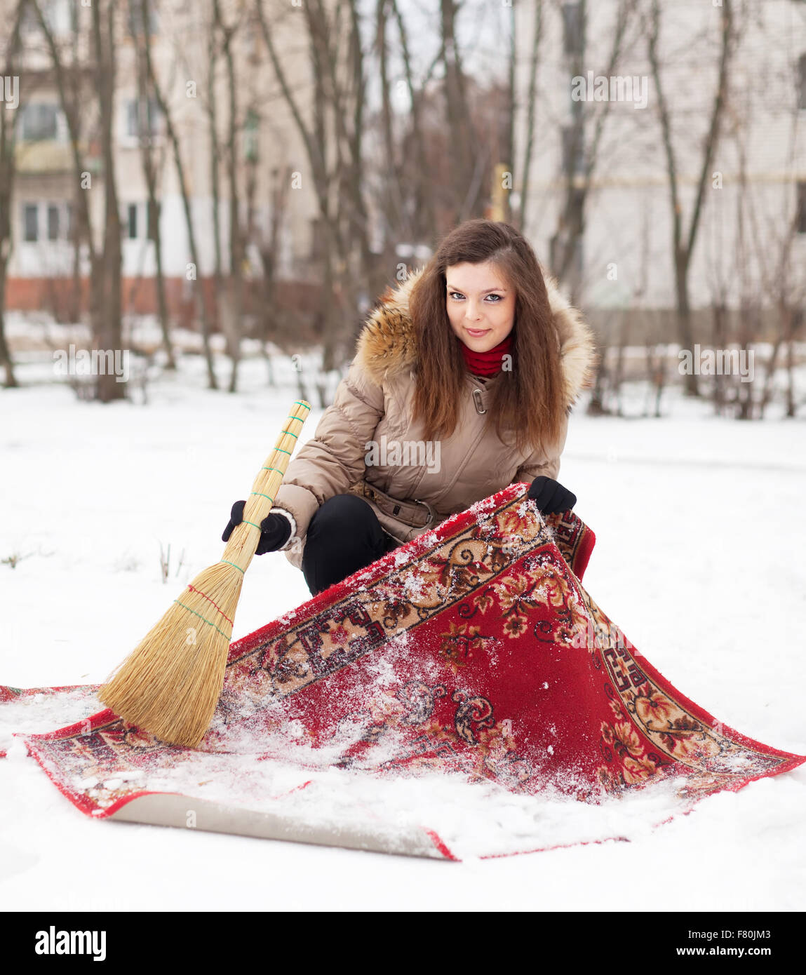 Lächelndes Mädchen reinigt Teppich mit Schnee im Wintertag im freien Stockfoto