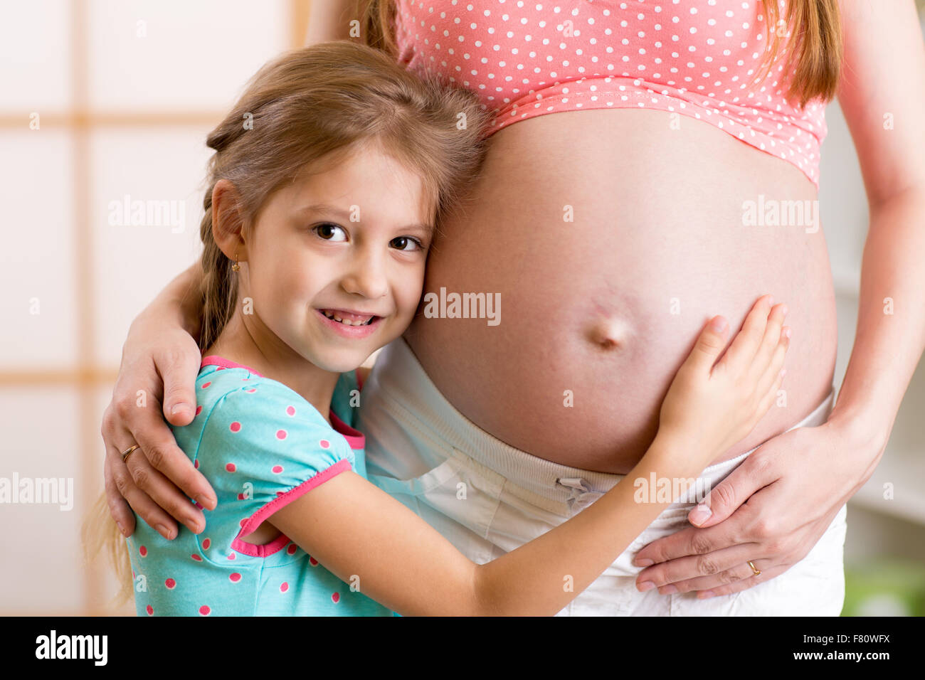 glückliches Kind Mädchen umarmt schwangere Mutter Bauch Stockfoto