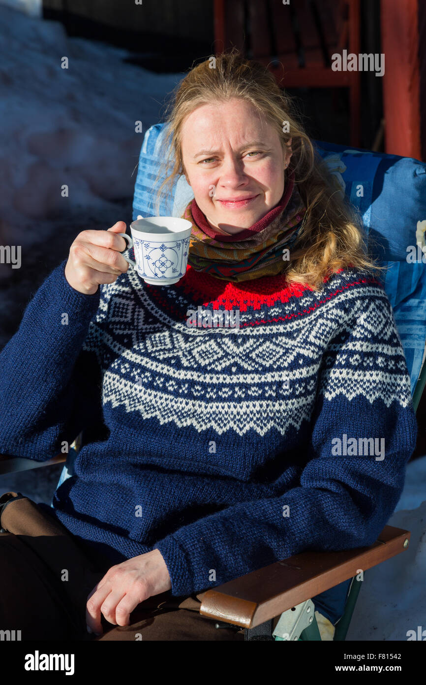 Nahaufnahme eines jungen ziemlich norwegische Frau genießen einige Wintersonne und eine Tasse Kaffee in einem traditionellen norwegischen jumper Stockfoto