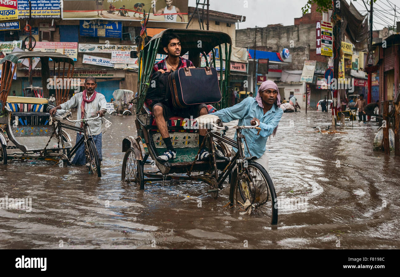 Fahrradrikscha transportiert Passagiere durch grelle Flut während schweren Monsunregen. Stockfoto