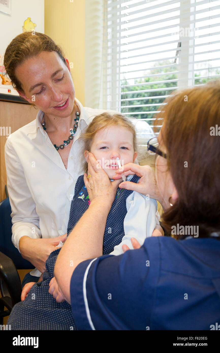 3 Jahre altes Kind mit ihrer Mutter / Mutter, erhält Dosis der Fluenz Grippe-Impfstoff Nasenspray Immunisierung von NHS Practice Nurse UK Stockfoto