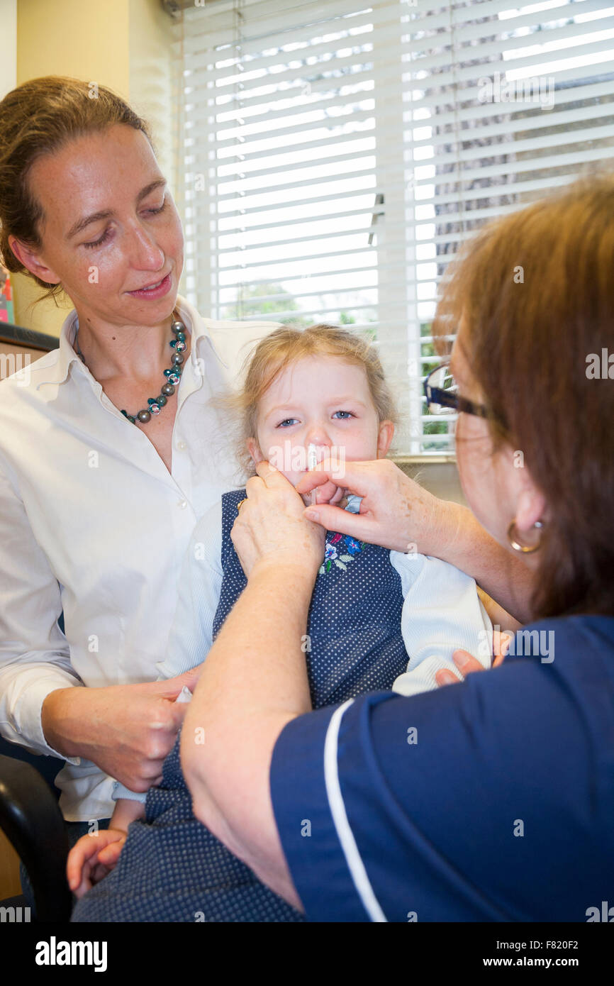 3 Jahre altes Kind mit ihrer Mutter / Mutter, erhält Dosis der Fluenz Grippe-Impfstoff Nasenspray Immunisierung von NHS Practice Nurse UK Stockfoto