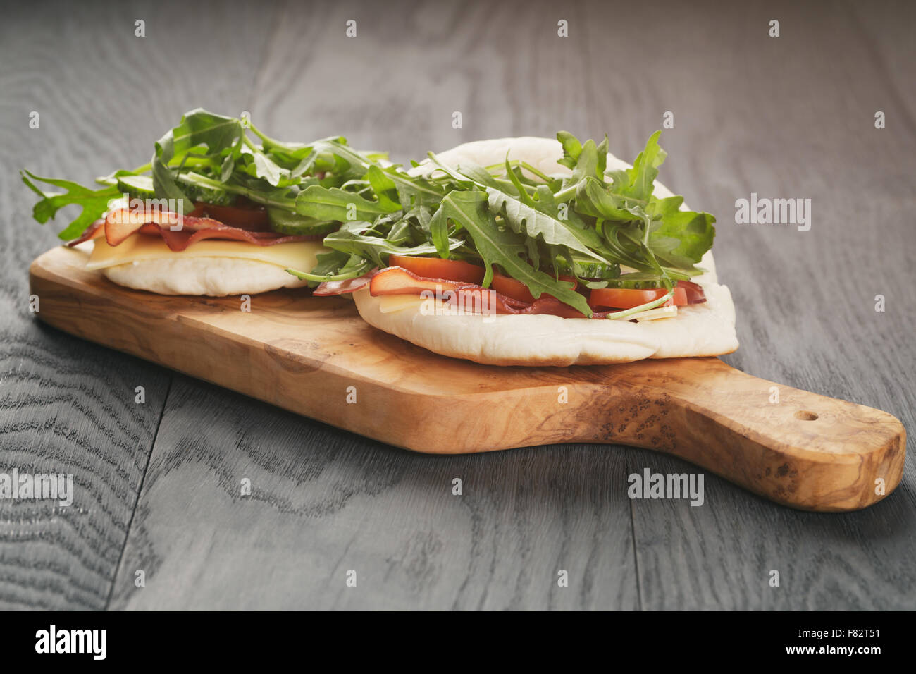 rustikale Sandwiches mit Schinken, Rucola und Tomaten im Fladenbrot auf Holztisch Stockfoto