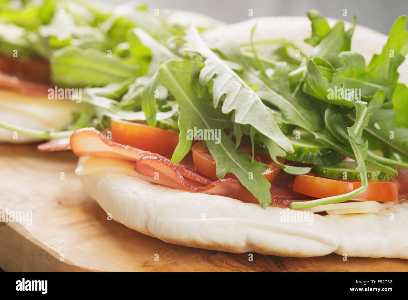 rustikale Sandwiches mit Schinken, Rucola und Tomaten im Fladenbrot auf Holztisch Stockfoto
