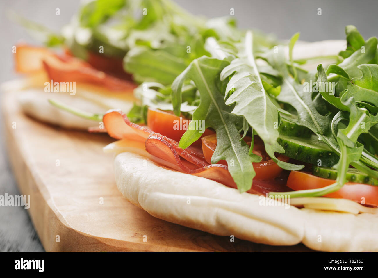 rustikale Sandwiches mit Schinken, Rucola und Tomaten im Fladenbrot auf Holztisch Stockfoto