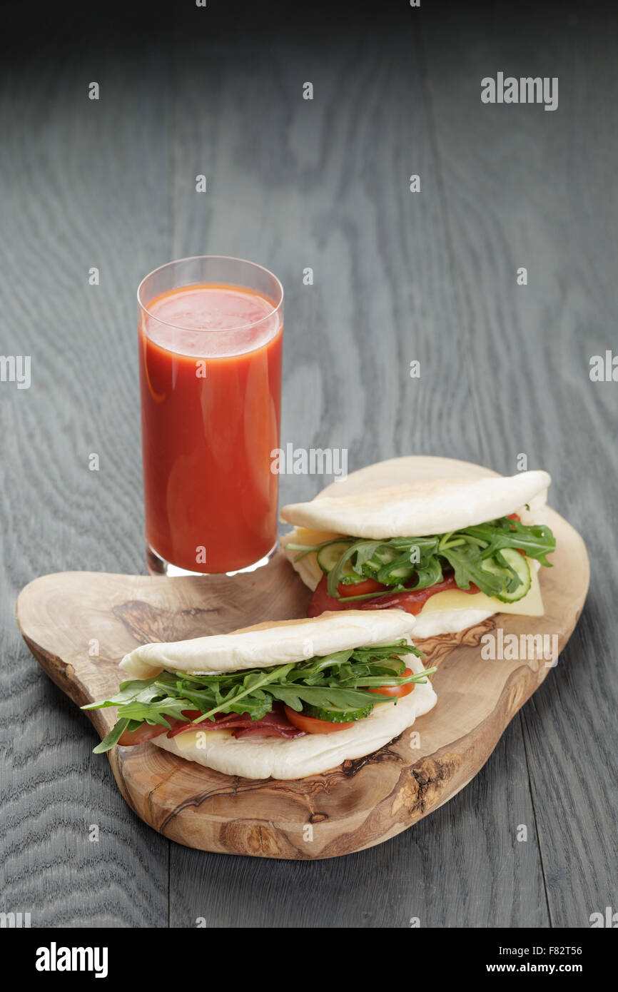 rustikale Sandwiches mit Schinken, Rucola und Tomaten im Fladenbrot auf Holztisch Stockfoto