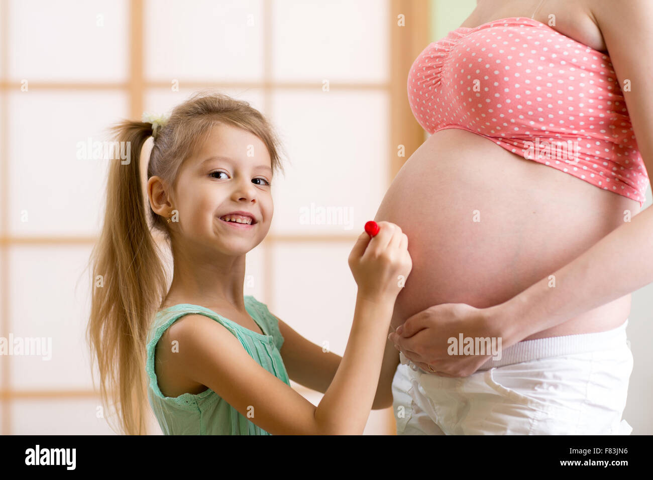 Niedliche kleine Mädchen malt auf den Bauch der schwangeren Mutter Stockfoto