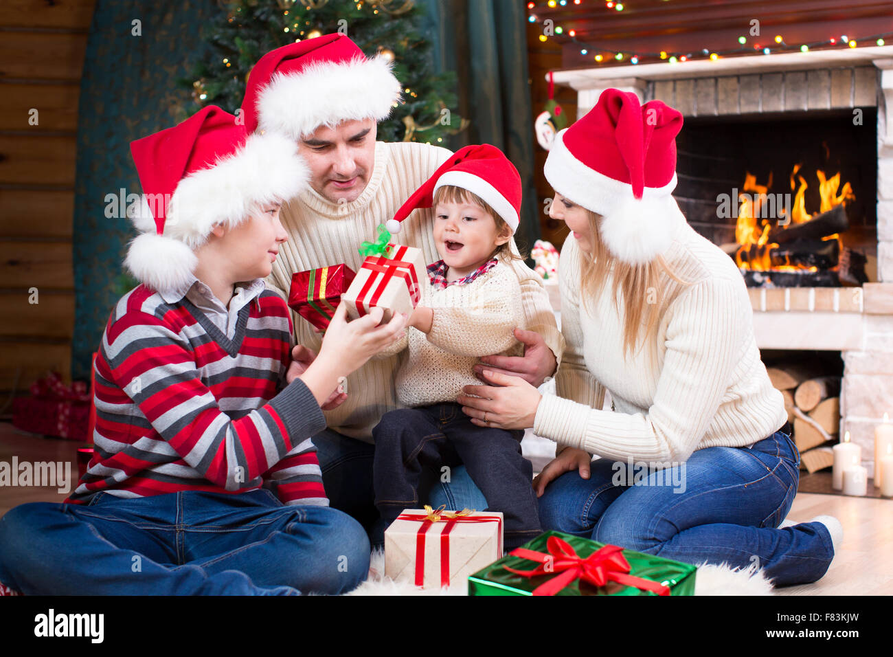 Happy Family im roten Hüte mit Geschenken am Weihnachtsbaum in der Nähe von Kamin sitzen Stockfoto