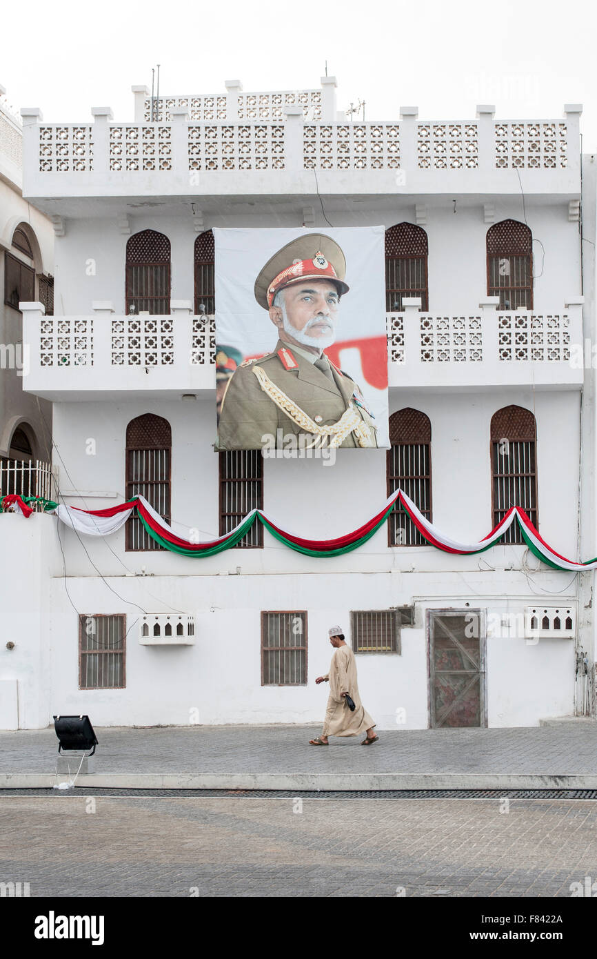 Mann zu Fuß vorbei an einem Gebäude geschmückt mit einem Plakat des Sultans von Oman in Mutrah in Muscat, der Hauptstadt des Oman. Stockfoto