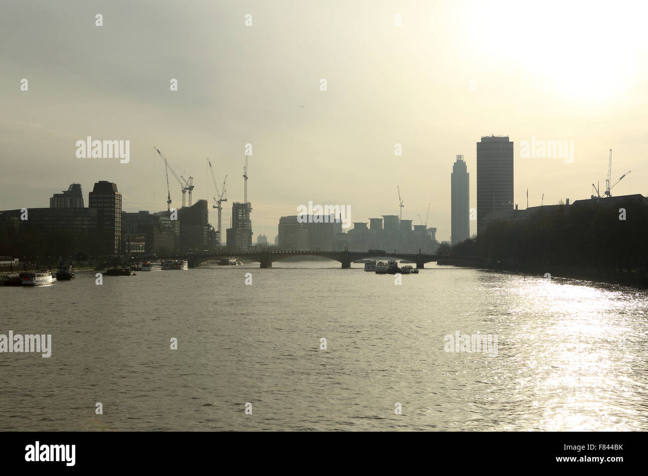 Sonne schimmert auf der Themse an einem trüben Tag in London, UK. Krane überragen am Flussufer Bauten von Lambeth Bridge. Stockfoto