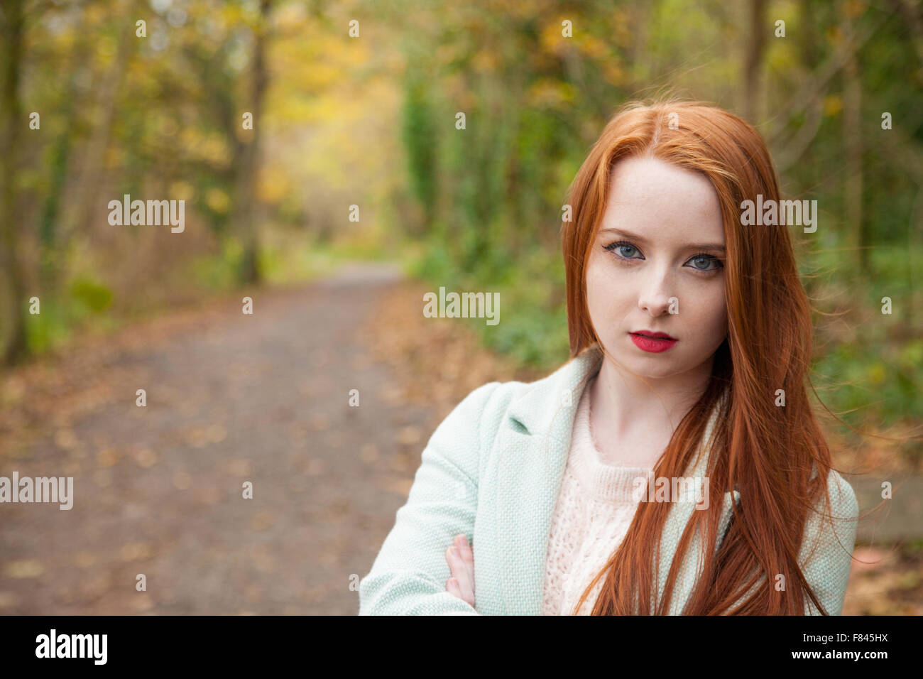 Rothaarige Frau außerhalb mit einem Waldweg im Hintergrund. Stockfoto