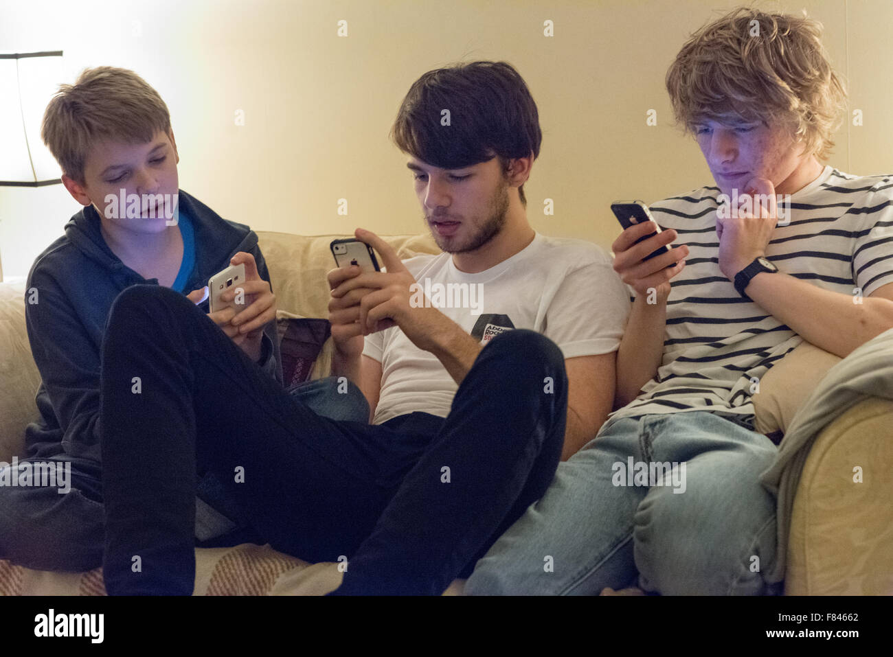Drei gut aussehende weiße glücklich Jungs im Teenageralter Lachen und Blick auf ihre Handys, Online-Spiele, YouTube anschauen und auf soziale meida Stockfoto