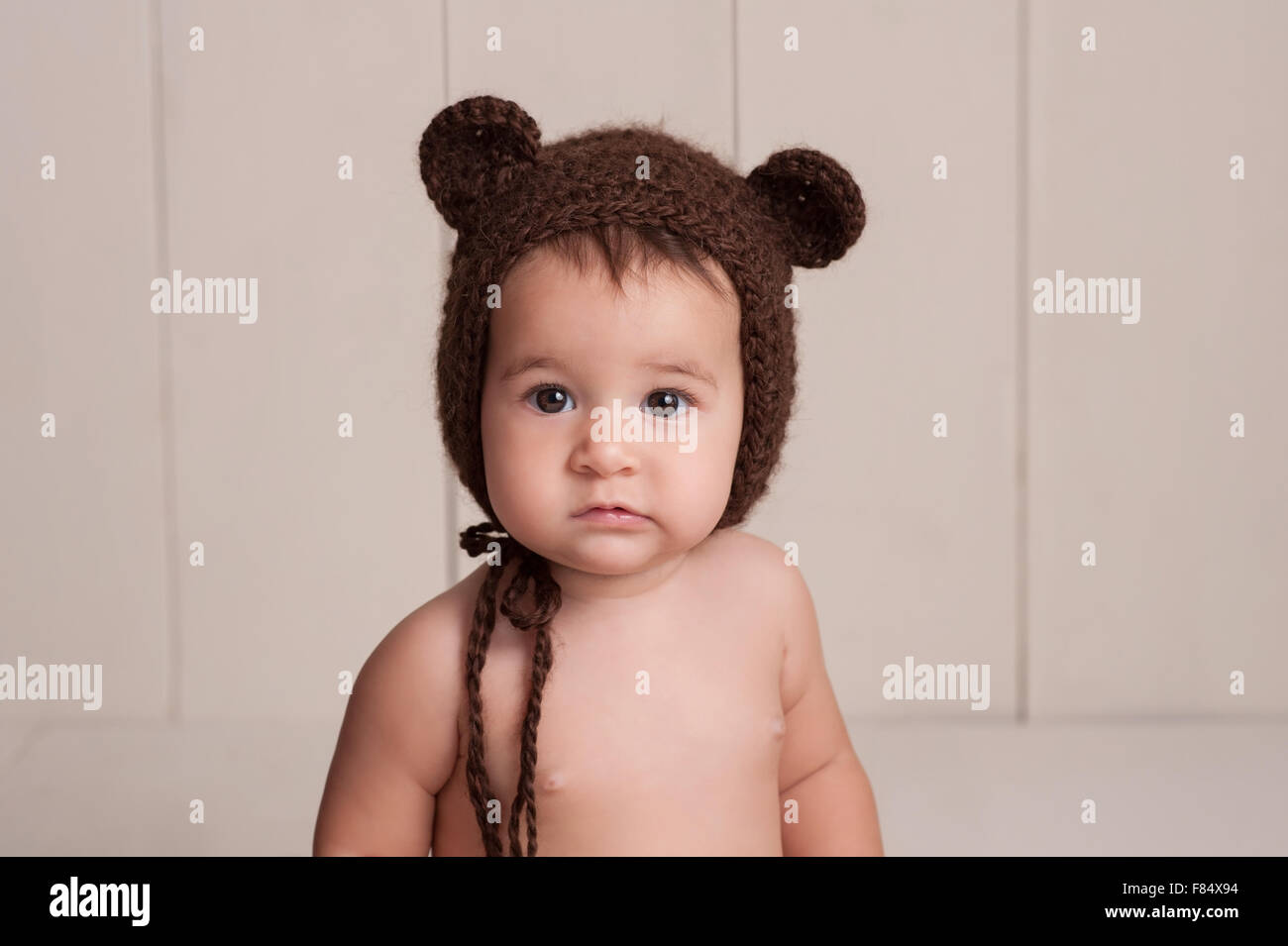 Kopfschuss von einem neun Monate alten Baby Mädchen trägt eine braune, gehäkelte, Bären-Motorhaube. Gedreht im Studio mit einem weißen, Holz getäfelten ba Stockfoto