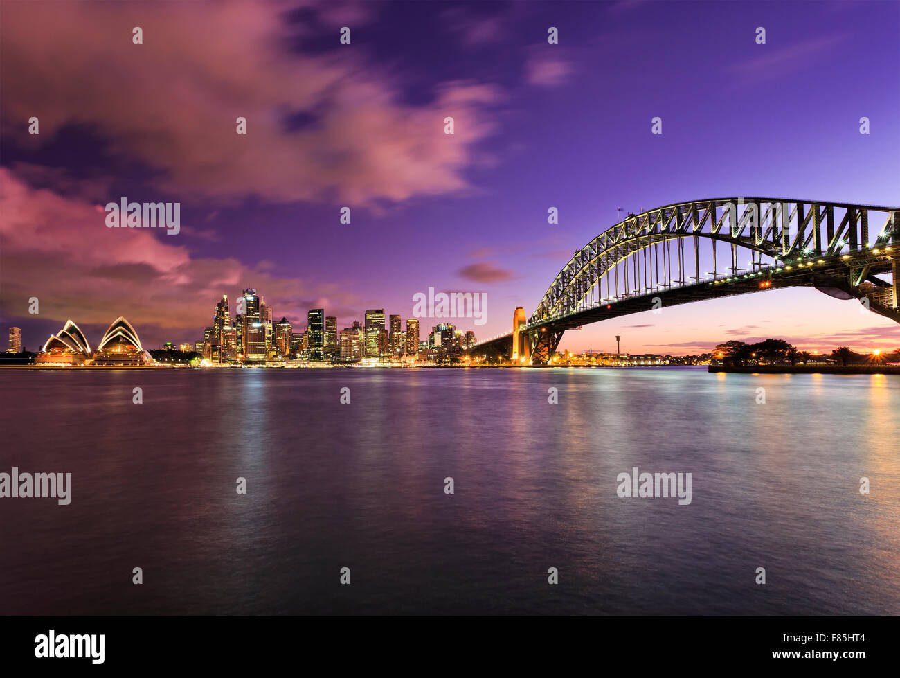 Wahrzeichen von Sydney bei Sonnenuntergang über den Harbour mit verschwommenen Wolken und Wasser reflektieren helle Lichter der bunte Beleuchtung Stockfoto