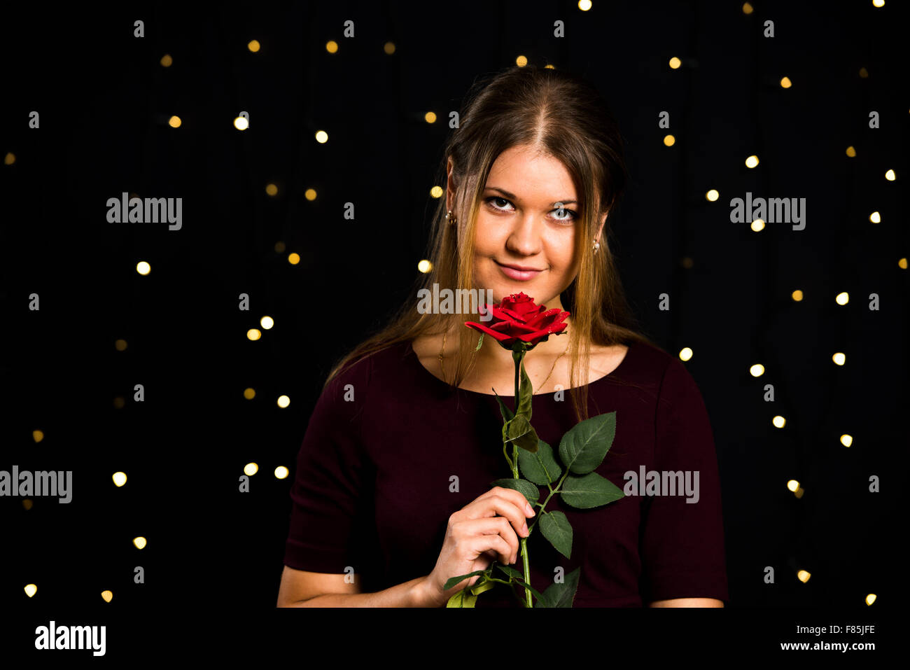 junge hübsche Frau auf schwarzem Hintergrund mit roten rose Stockfoto