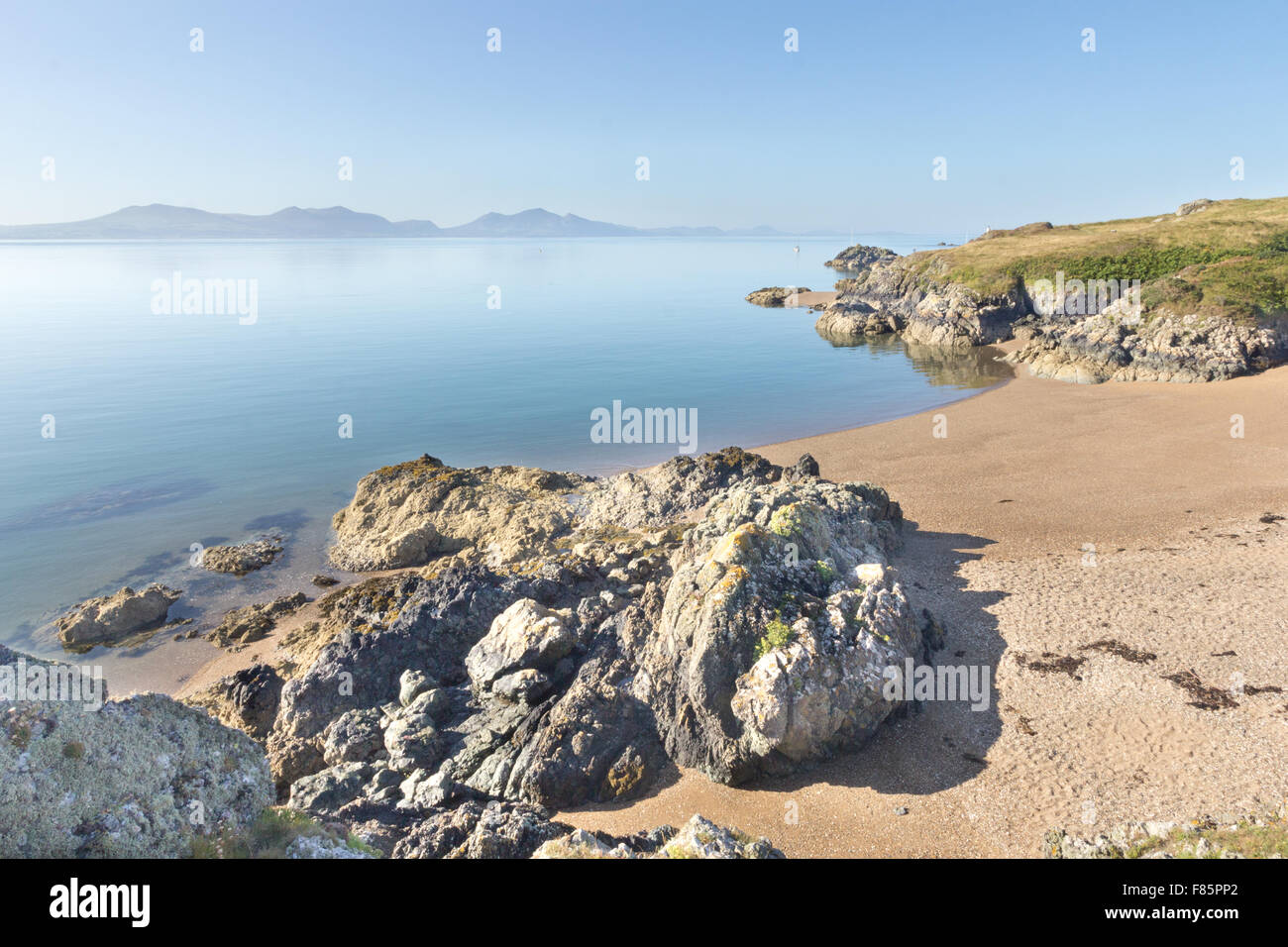 Vulkangestein und Strand auf Llanddwyn Island, Anglesey, Wales mit Halbinsel Llyn im Hintergrund Stockfoto