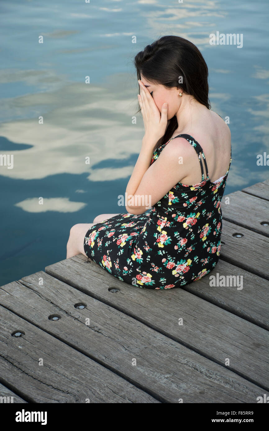 Elende junge Frau verbirgt ihr Gesicht auf dem Steg am Meer Stockfoto