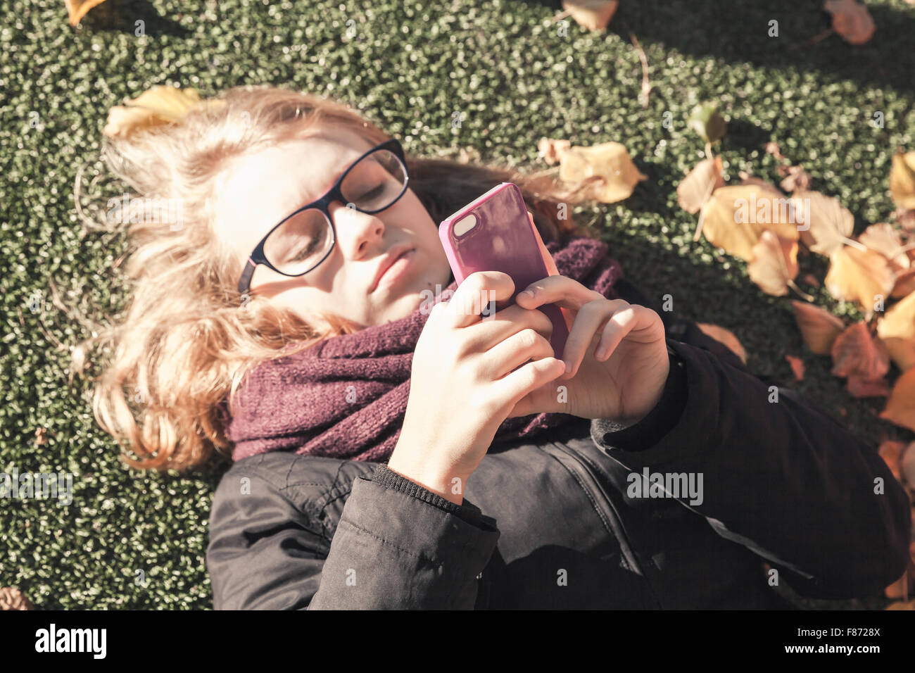 Kaukasische blonde Teenager-Mädchen im herbstlichen Park und mittels Smartphone, Vintage-Stil-Tonwertkorrektur-Foto-filter Stockfoto