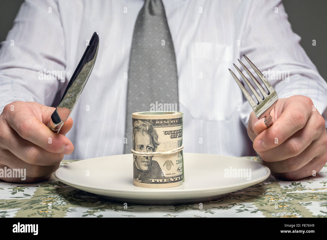 Geschäftsmann sitzt hinter einem Tisch mit Gabel und Messer bereit, ein Bündel von Dollar Essen serviert auf Teller - Business-Konzept Stockfoto