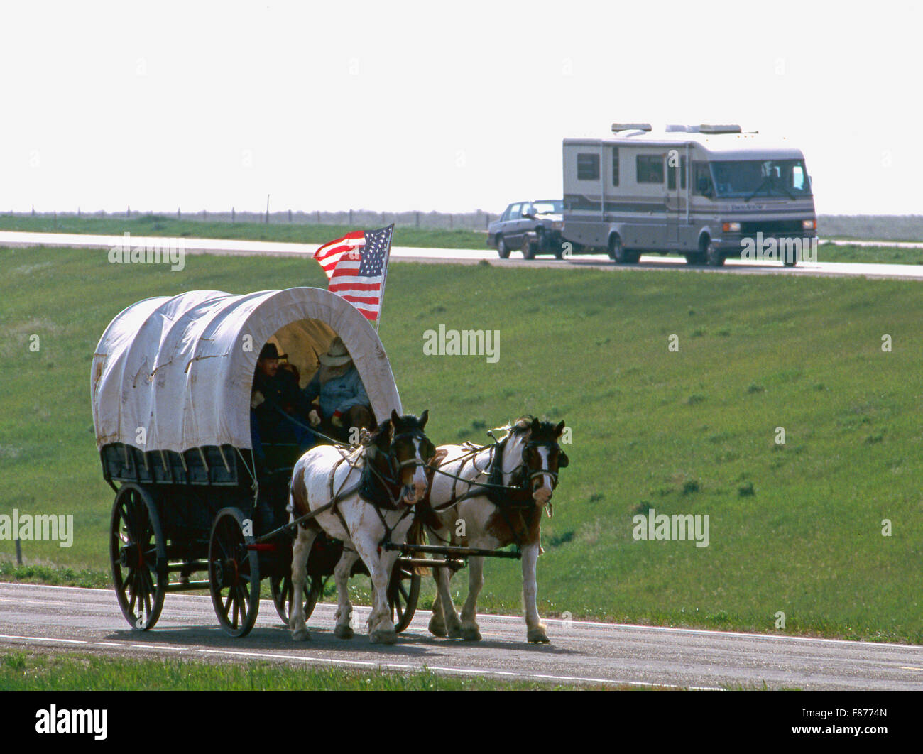 Ein Freizeitfahrzeug übergibt Planwagen und Reiter in der modernen South Dakota Prärie außerhalb Rapid City. Stockfoto