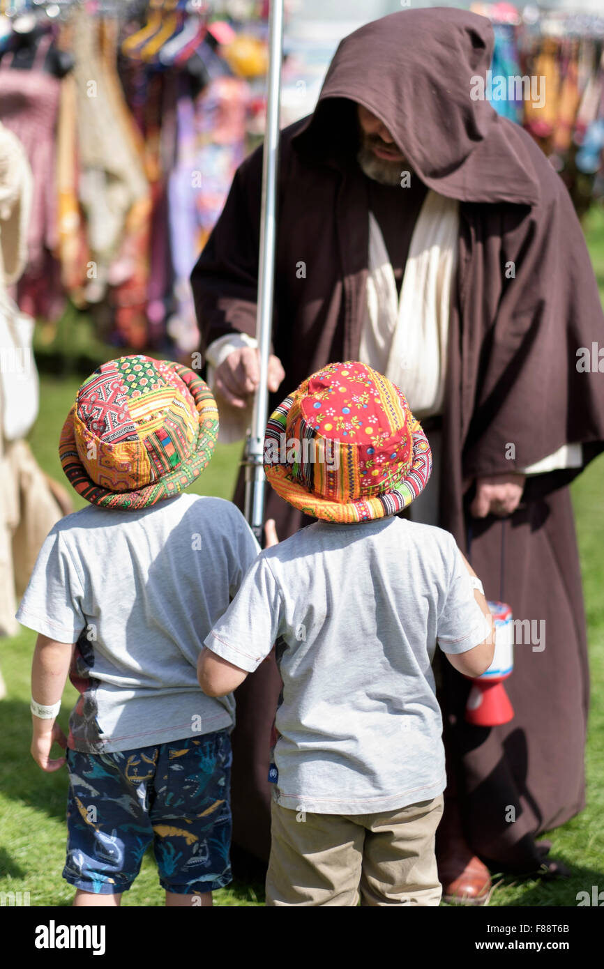 Mann gekleidet wie Obi-wan Kenobi Star Wars Charakter unterhält zwei junge Kinder mit bunten hüten Stockfoto