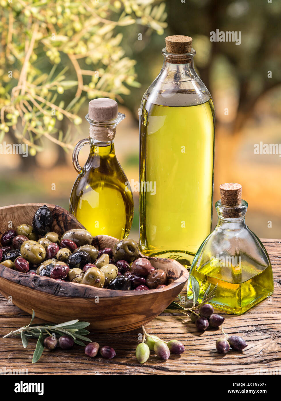 Olivenöl und Beeren sind auf dem Holztisch unter dem Olivenbaum. Stockfoto