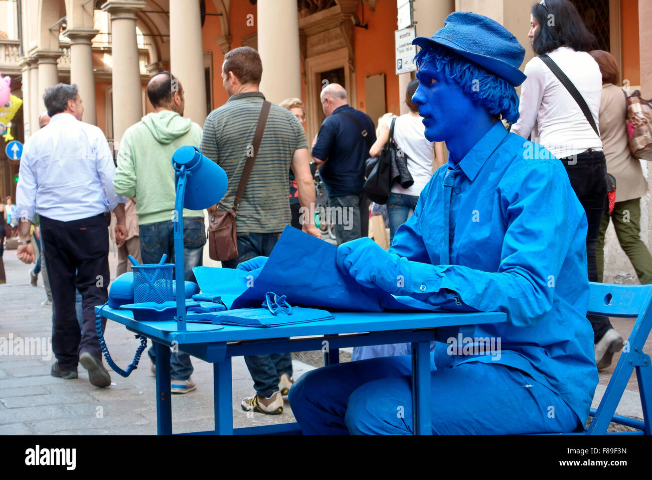 Blau gemalter Mann Straße Performer, menschliche Statue, sitzen noch an einem Schreibtisch, auf einer belebten Straße. Büro auf der Straße. Bologna, Emilia Romagna, Italien, EU Stockfoto