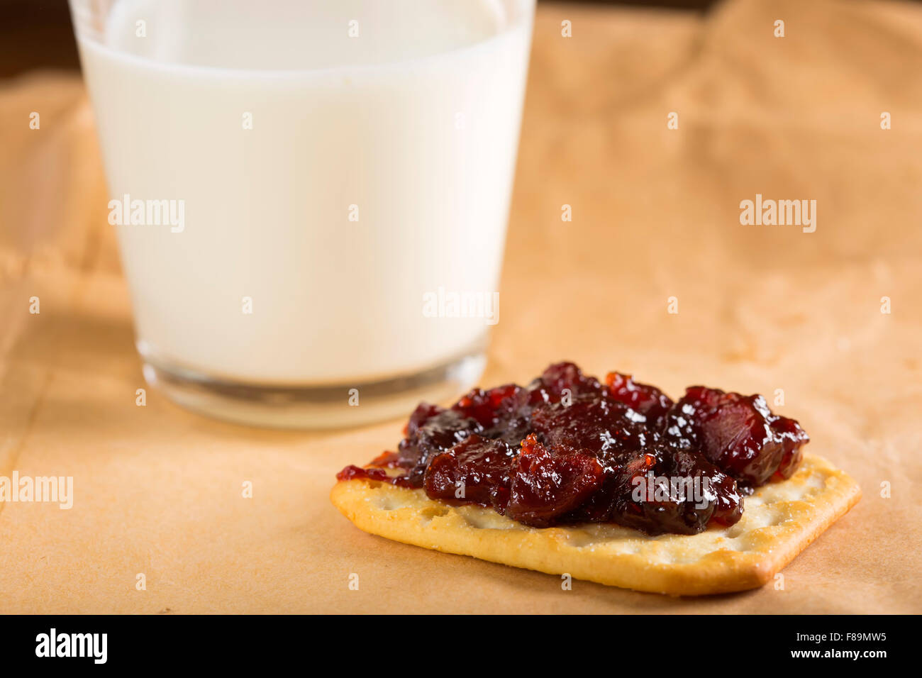 Quitten Marmelade auf Saltine Cracker mit einem Glas Milch auf Papier Stockfoto