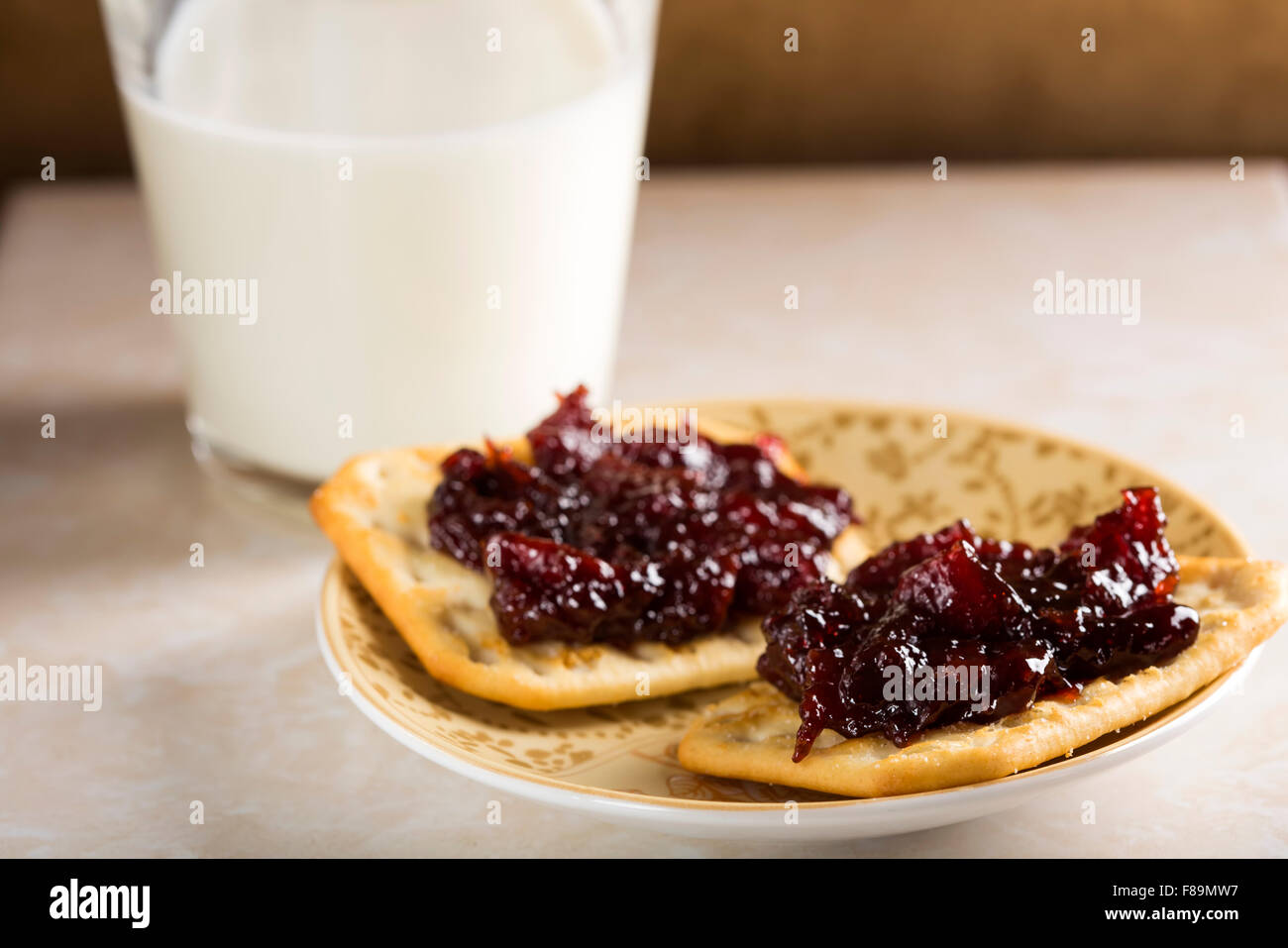 Zwei Kekse mit Quitten Marmelade auf einem Teller und einem Glas Milch Stockfoto