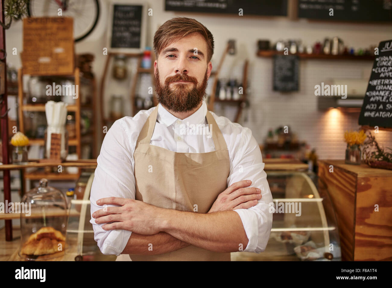 Porträt des jungen Mannes trägt Schürze stehend mit seinen Armen überquerte in einem Café. Kaukasischen Mann mit Bart stehen in einem café Stockfoto