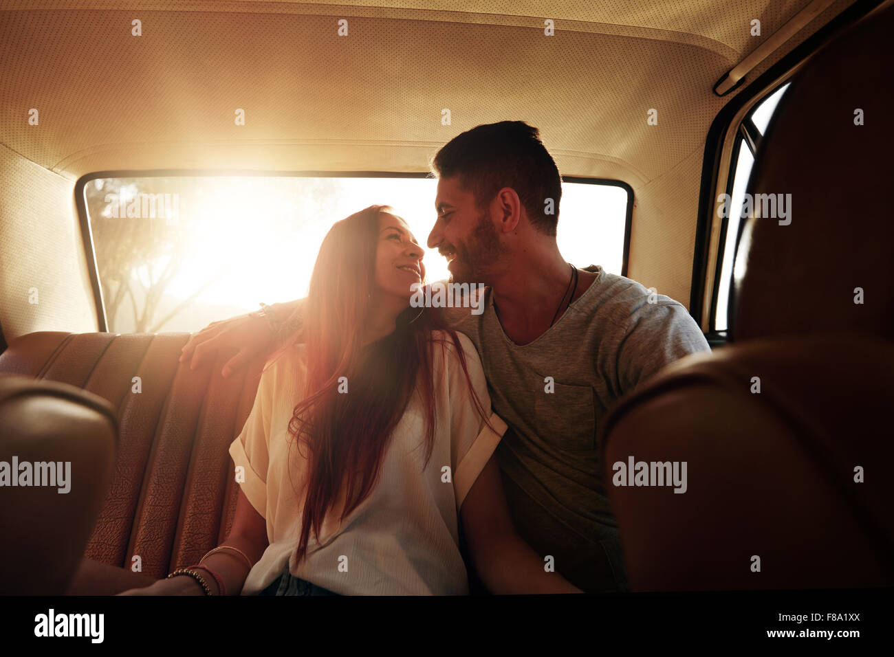 Glückliches Paar Road trip. Junger Mann und Frau sitzen auf der Rückbank des Autos sahen einander lächelnd an einem Sommertag. Stockfoto