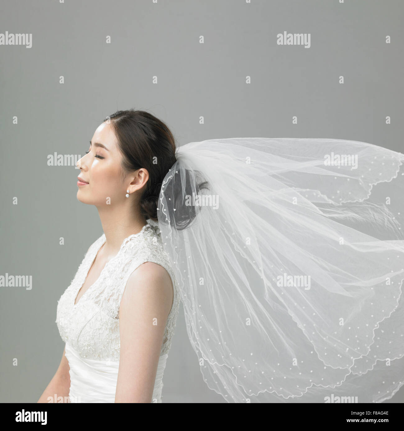 Koreanische Braut in weht Hochzeitsschleier mit geschlossenen Augen Stockfoto
