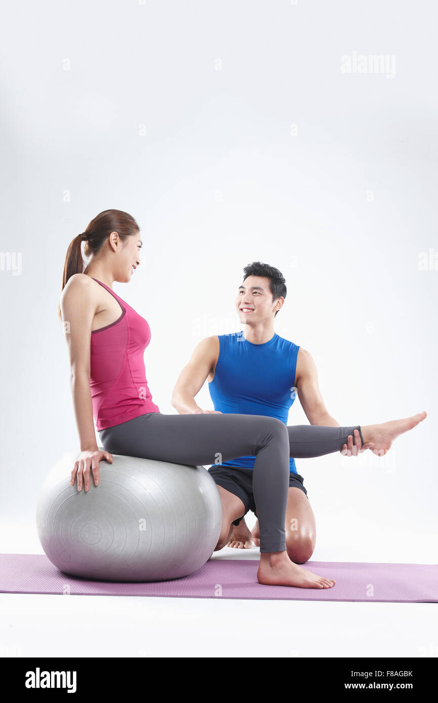 Frau lehnt sich zurück auf Gymnastikball und heben ein Bein von coaching ihr Mann gehalten Stockfoto