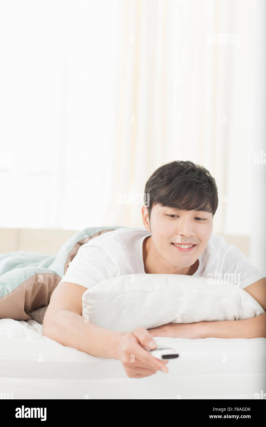Mann auf dem Bauch auf dem Bett liegend und mit Hilfe der Fernbedienung Stockfoto