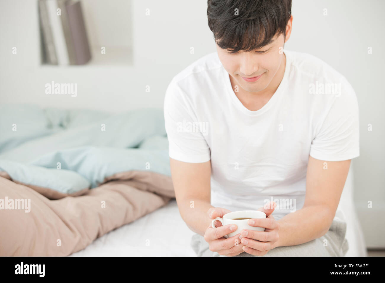 Mann sitzt auf dem Bett mit einer Tasse Kaffee in der Hand Stockfoto