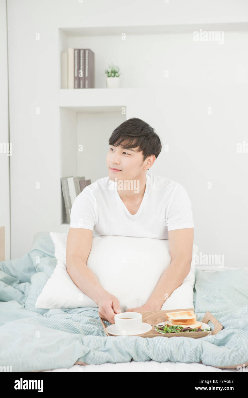 Platzieren eine Kissen unter den Arm und sitzen im Bett mit dem Frühstückstablett Mann Stockfoto