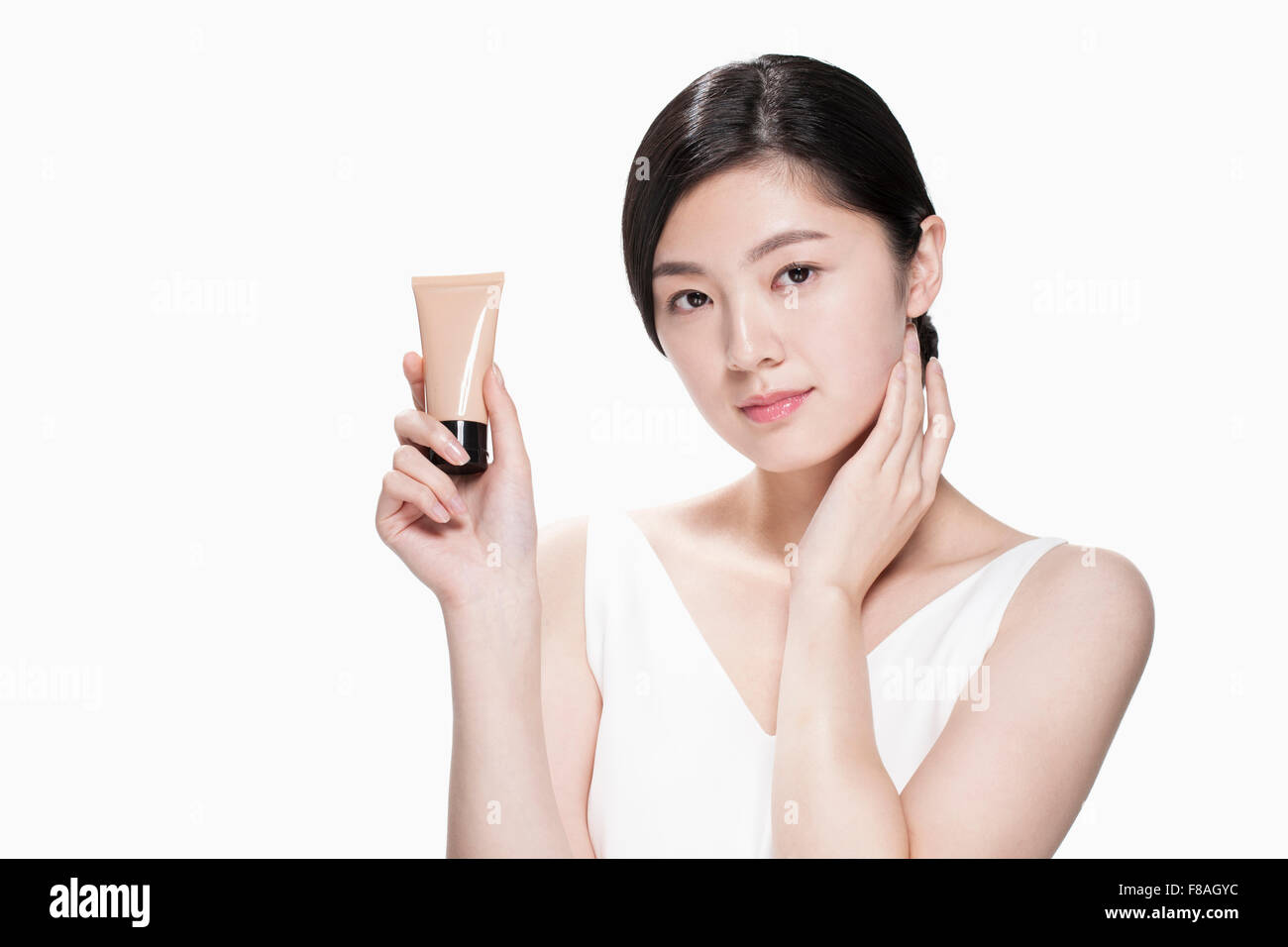 Junge asiatische Frau hält eine Tube Make-up-Produkt und den Hals mit der anderen Hand berühren Stockfoto