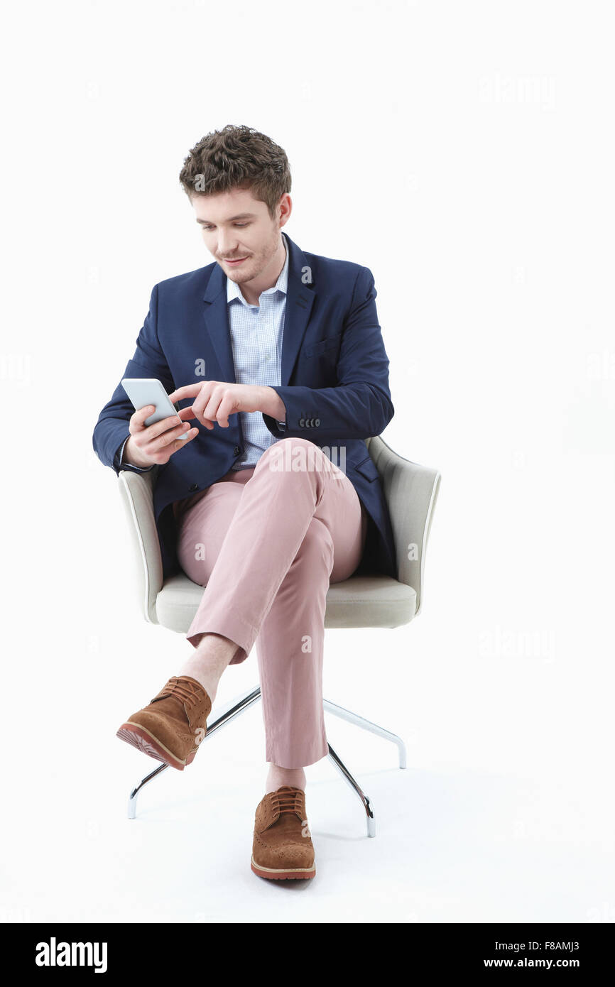 Geschäftsmann, sitzen mit den Beinen gekreuzt und mit Smartphone auf Stuhl Stockfoto
