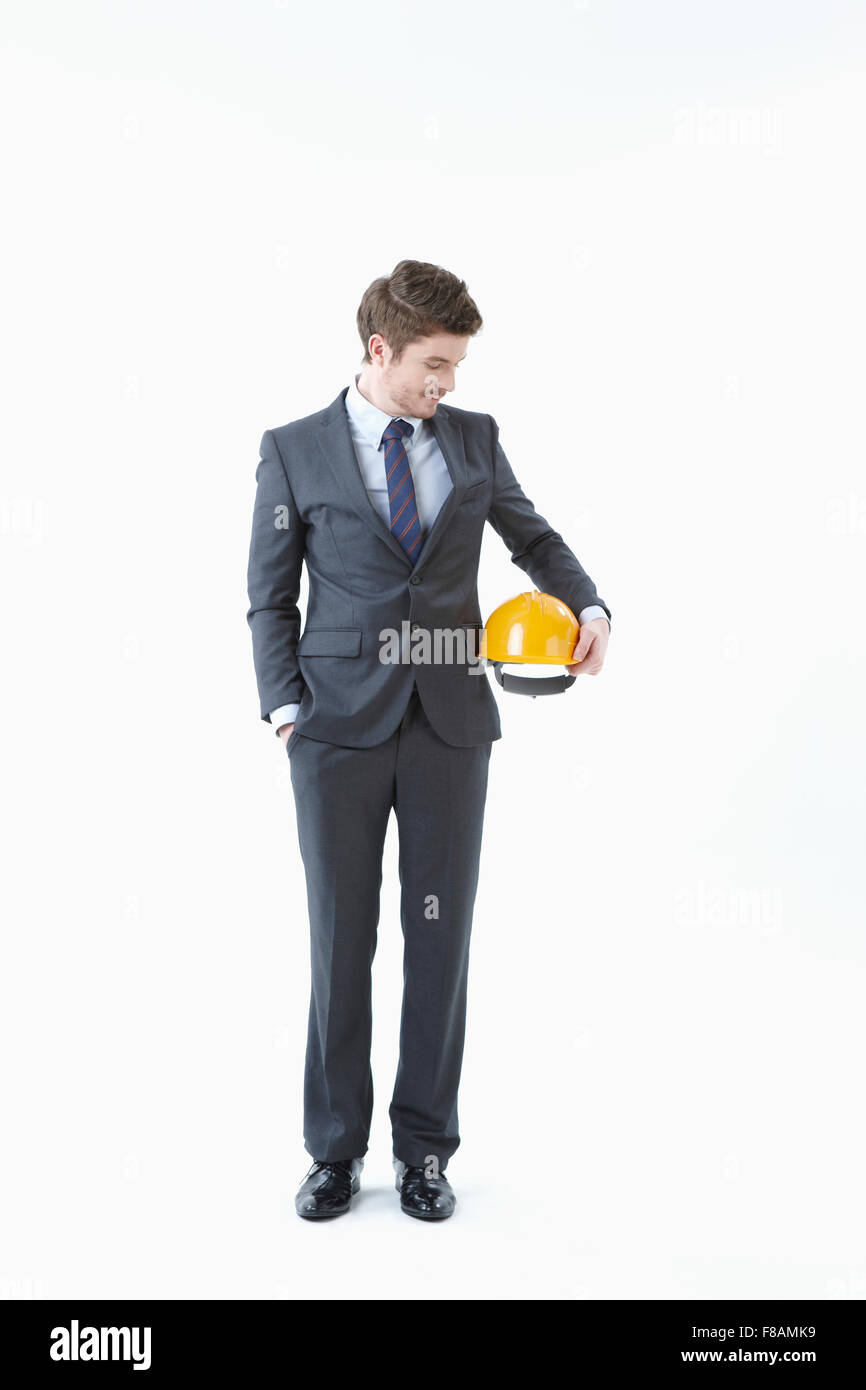 Zuversichtlich Geschäftsmann stehend mit Hand in der Tasche, hält einen Helm und blickte auf Sie Stockfoto