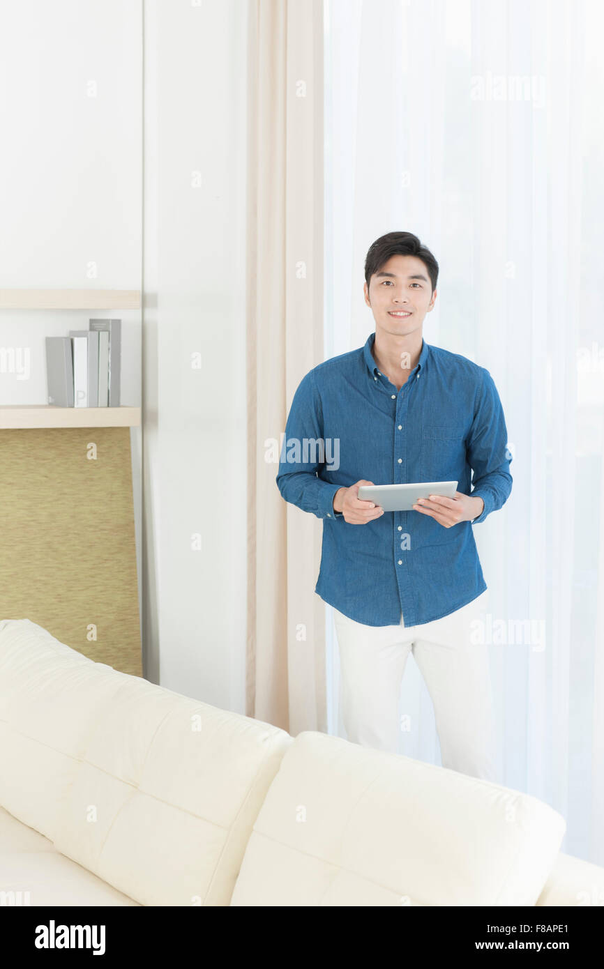 Jungen Mann hält eine Tablette vorne vor dem Fenstervorhang starrte lächelnd Stockfoto