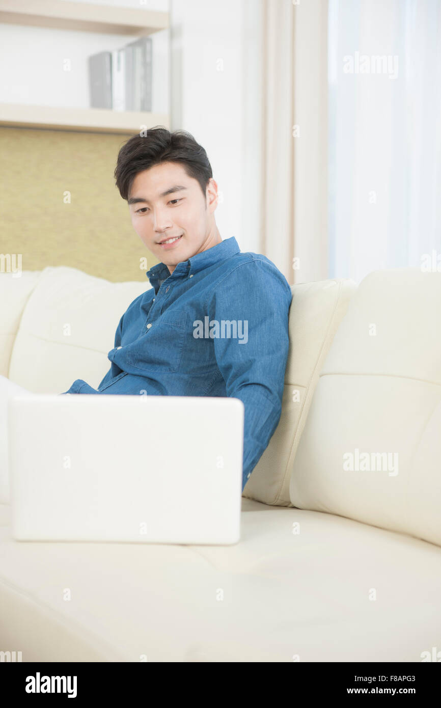 Lächelnd jungen Mann auf der Suche nach einem Notebook auf sofa Stockfoto