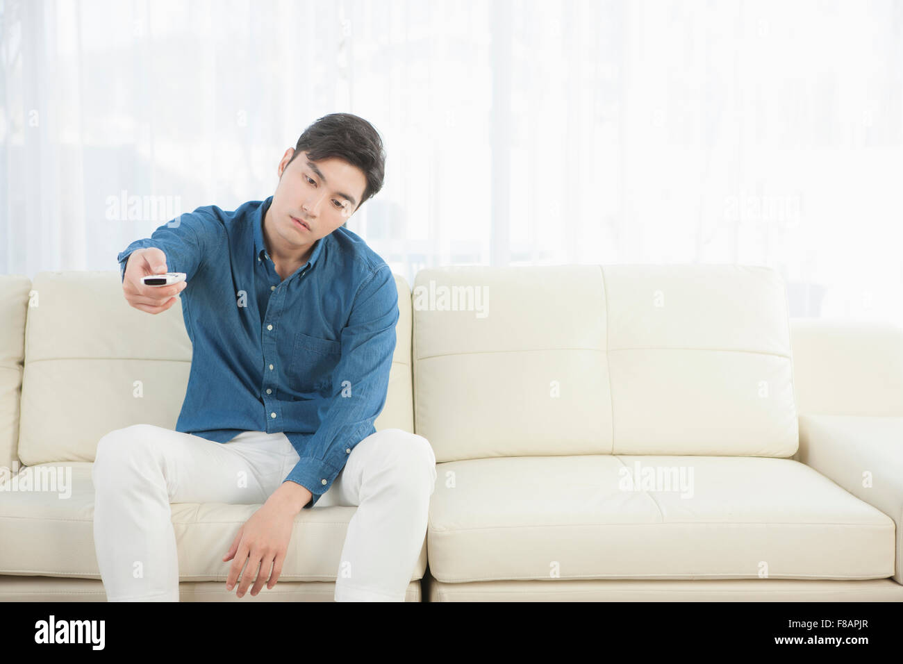 Junger Mann sucht langweilig hält eine Fernbedienung auf sofa Stockfoto