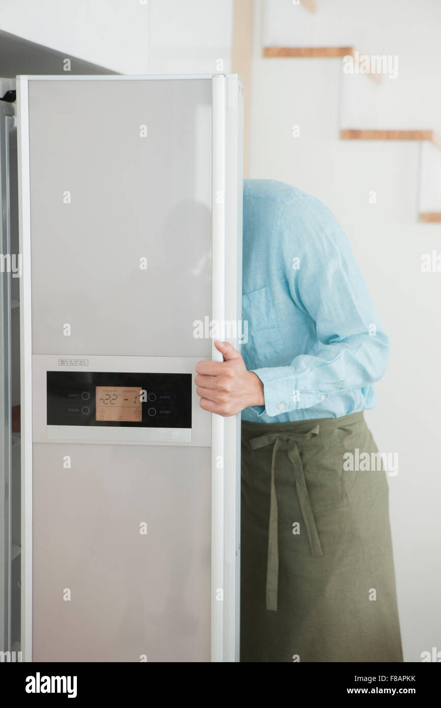 Seitenansicht des Yong Mann trägt eine Schürze und Eröffnung Kühlschrank Stockfoto