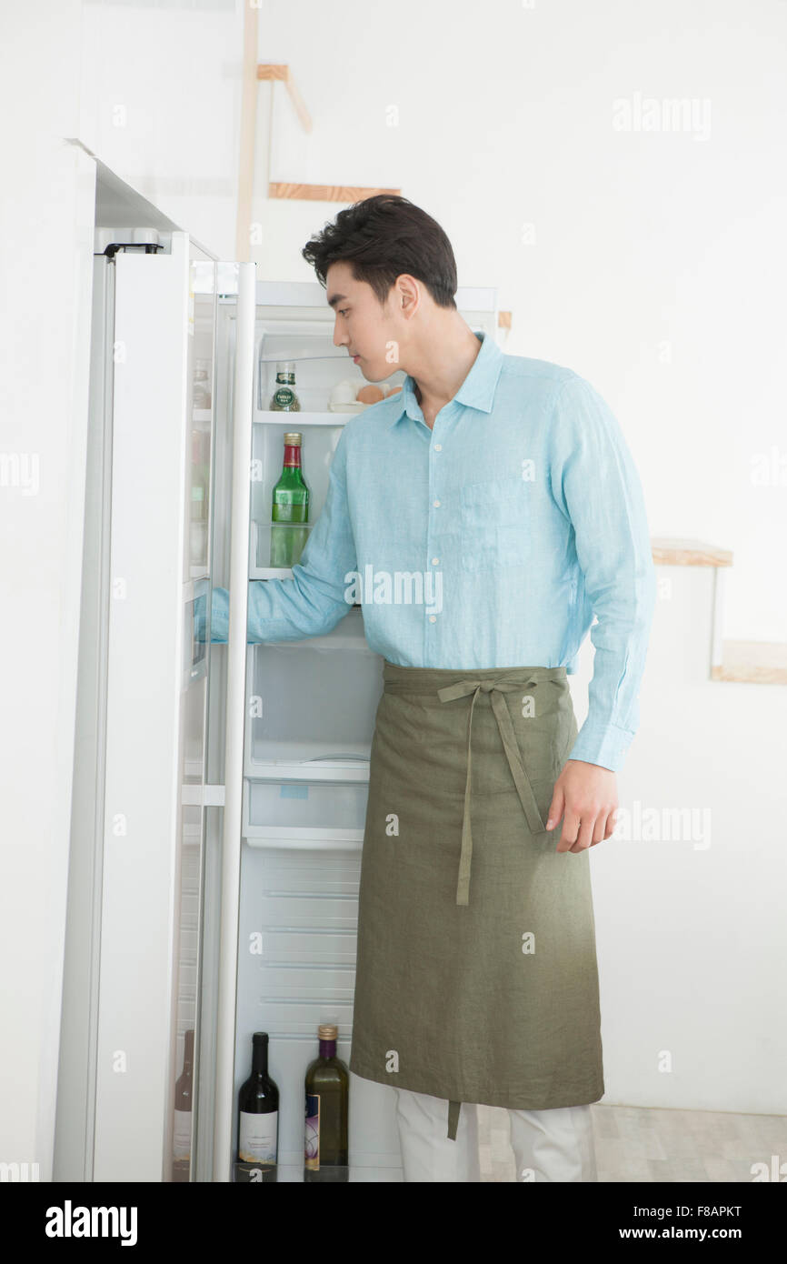 Seitenansicht der junge Mann trägt eine Schürze, die auf der Suche im Kühlschrank Stockfoto