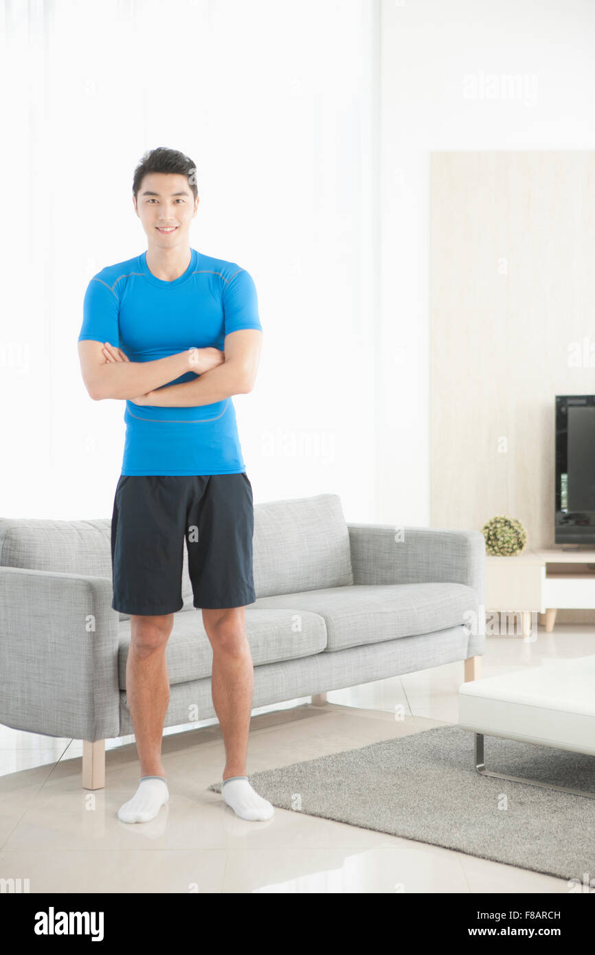 Mann in Sportbekleidung steht mit verschränkten Armen im Wohnzimmer starrte auf Vorderseite Stockfoto